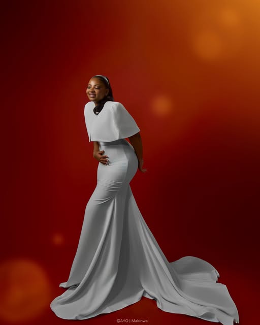 Ivory sculptural gown with cape shoulders and a long train, against a red studio backdrop